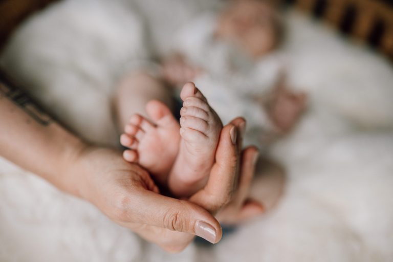 Winzige Babyfüße werden sanft von den liebevollen Händen der Mutter gehalten, eingefangen von Kathy Audrey Photography.