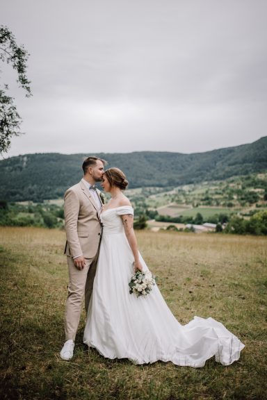 Zärtlicher Hochzeitskuss: Braut und Bräutigam auf einer grünen Wiese, Kuss auf die Stirn, fotografiert von Kathy Audrey Photography.