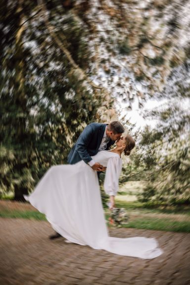 Inniger Hochzeitskuss: Braut und Bräutigam in dynamischer Pose, unscharfer Hintergrund, eingefangen von Kathy Audrey Photography.