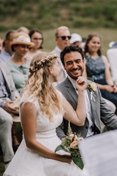 Brautpaar neckt sich während der Trauung, umgeben von lächelnden Familienmitgliedern und Freunden, fotografiert von Kathy Audrey Photography