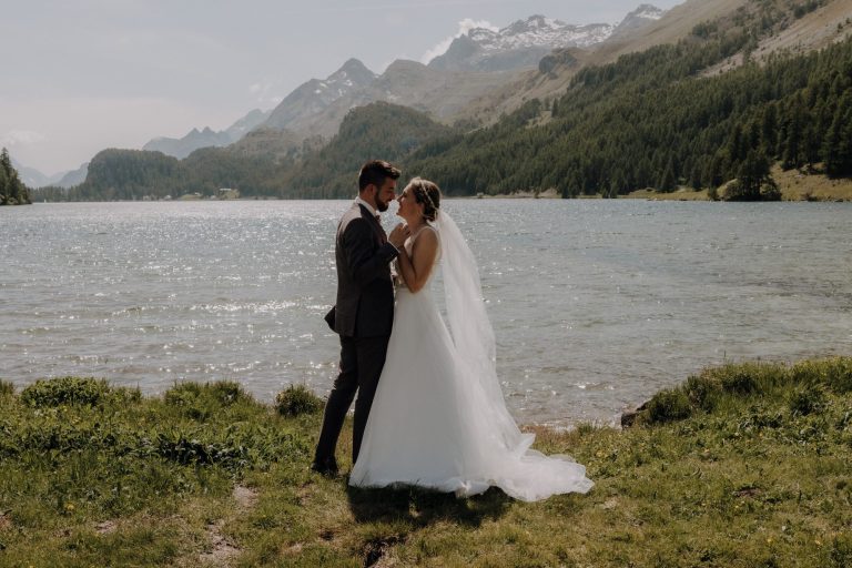 Hochzeitspaar steht romantisch am See, grüne Wiese und Berge im Hintergrund | by Kathyaudrey Photography