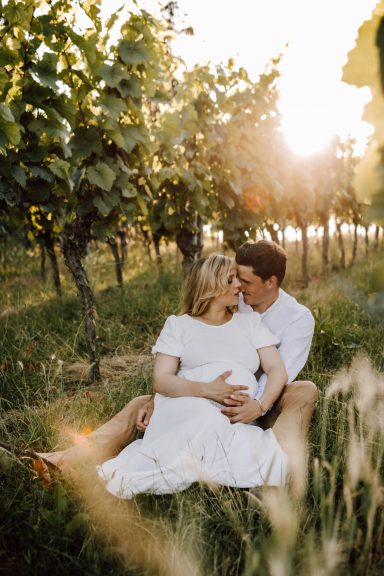 Schwangeres Liebespaar sitzt zwischen Weinreben, Sonnenuntergang, küssen sich beinahe, Kathy Audrey Photography